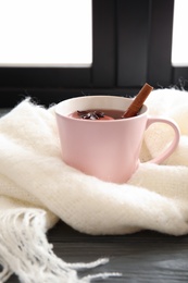 Photo of Cup of hot winter drink with knitted scarf near window. Cozy season