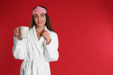 Young woman in bathrobe with cup of coffee on red background. Space for text