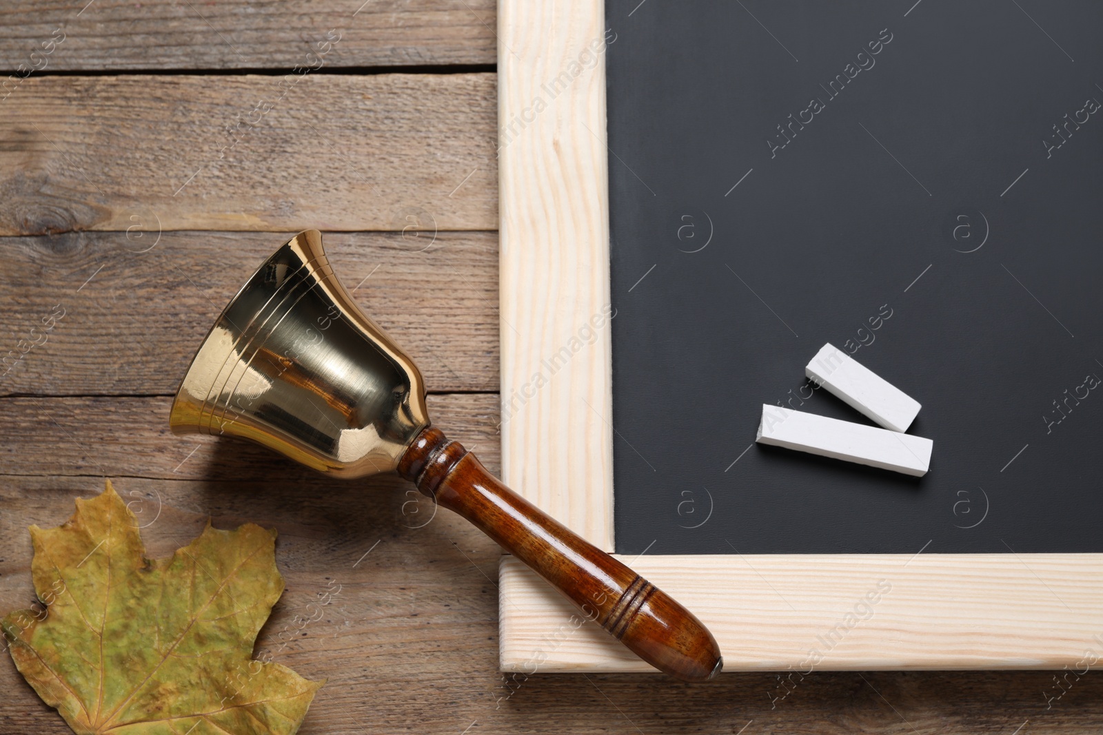 Photo of Golden school bell, autumn leaf and blackboard with pieces of chalk on wooden table, flat lay