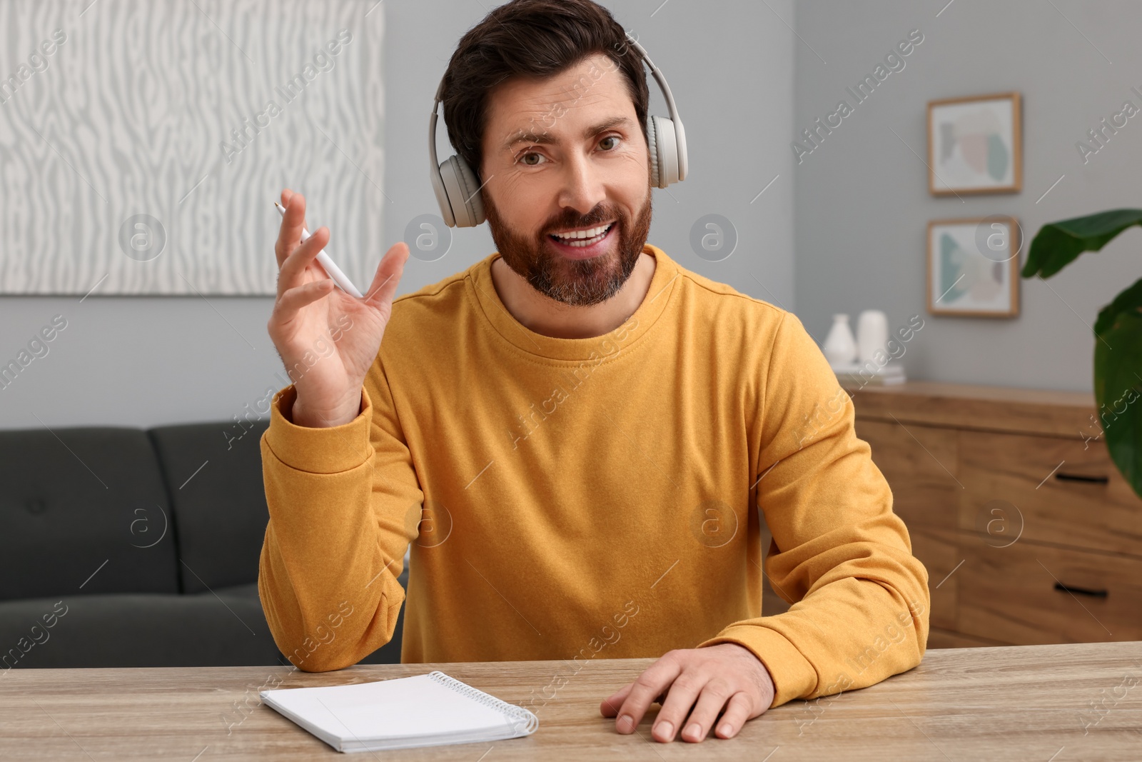 Photo of Man in headphones talking to someone at wooden table indoors