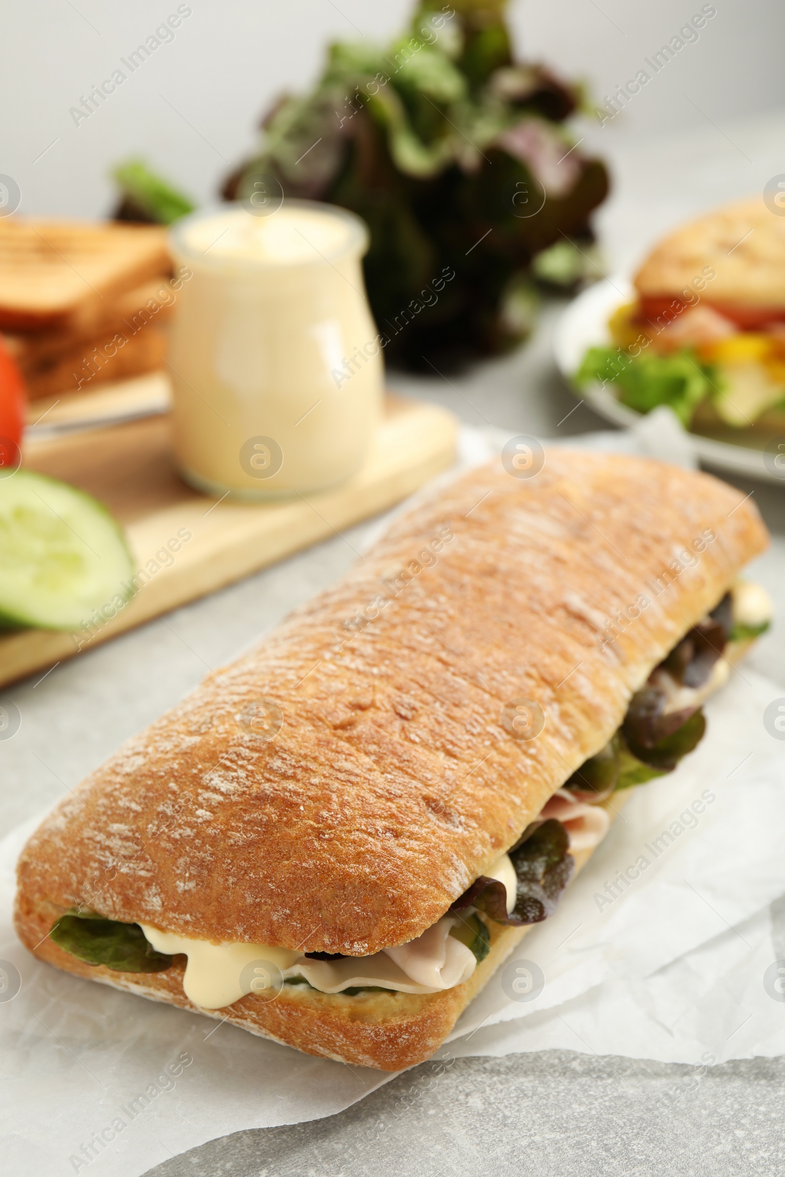 Photo of Delicious sandwich with vegetables, ham and mayonnaise on grey table, closeup