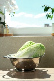 Photo of Fresh Chinese cabbages in colander on light wooden table indoors