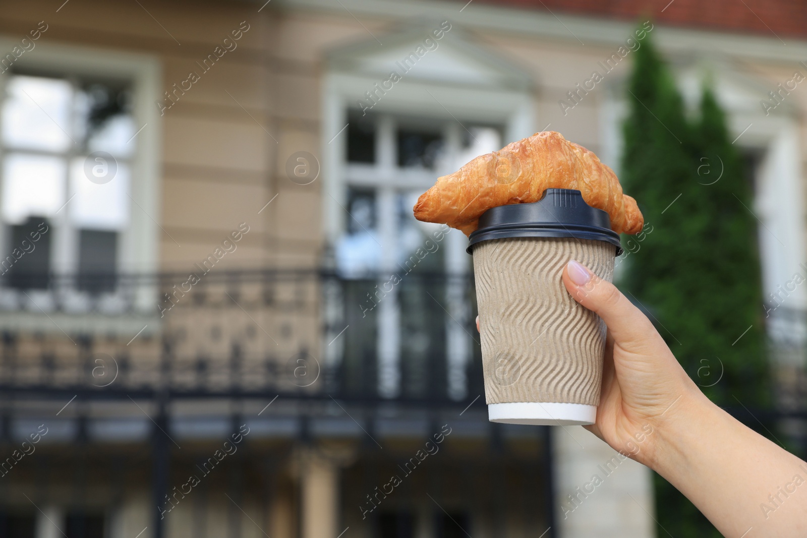 Photo of Woman holding croissant and paper cup in hand outdoors, closeup. Space for text