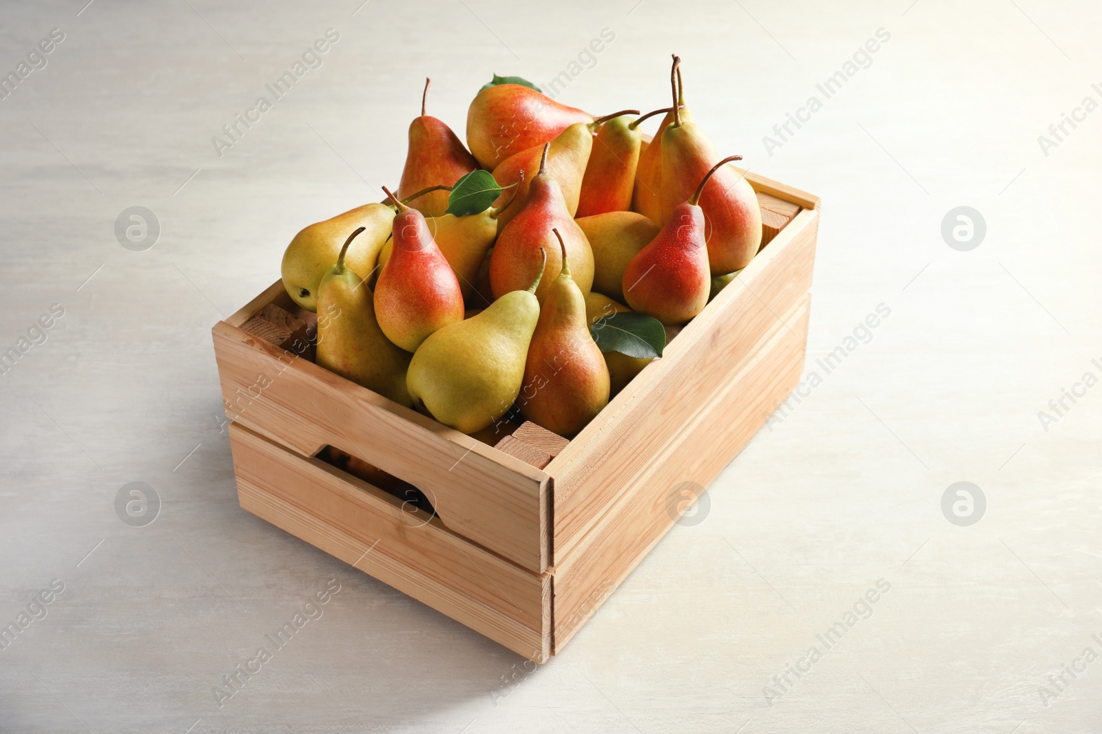 Photo of Wooden crate with ripe pears on light background