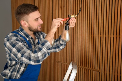 Electrician with screwdriver repairing ceiling lamp indoors. Space for text