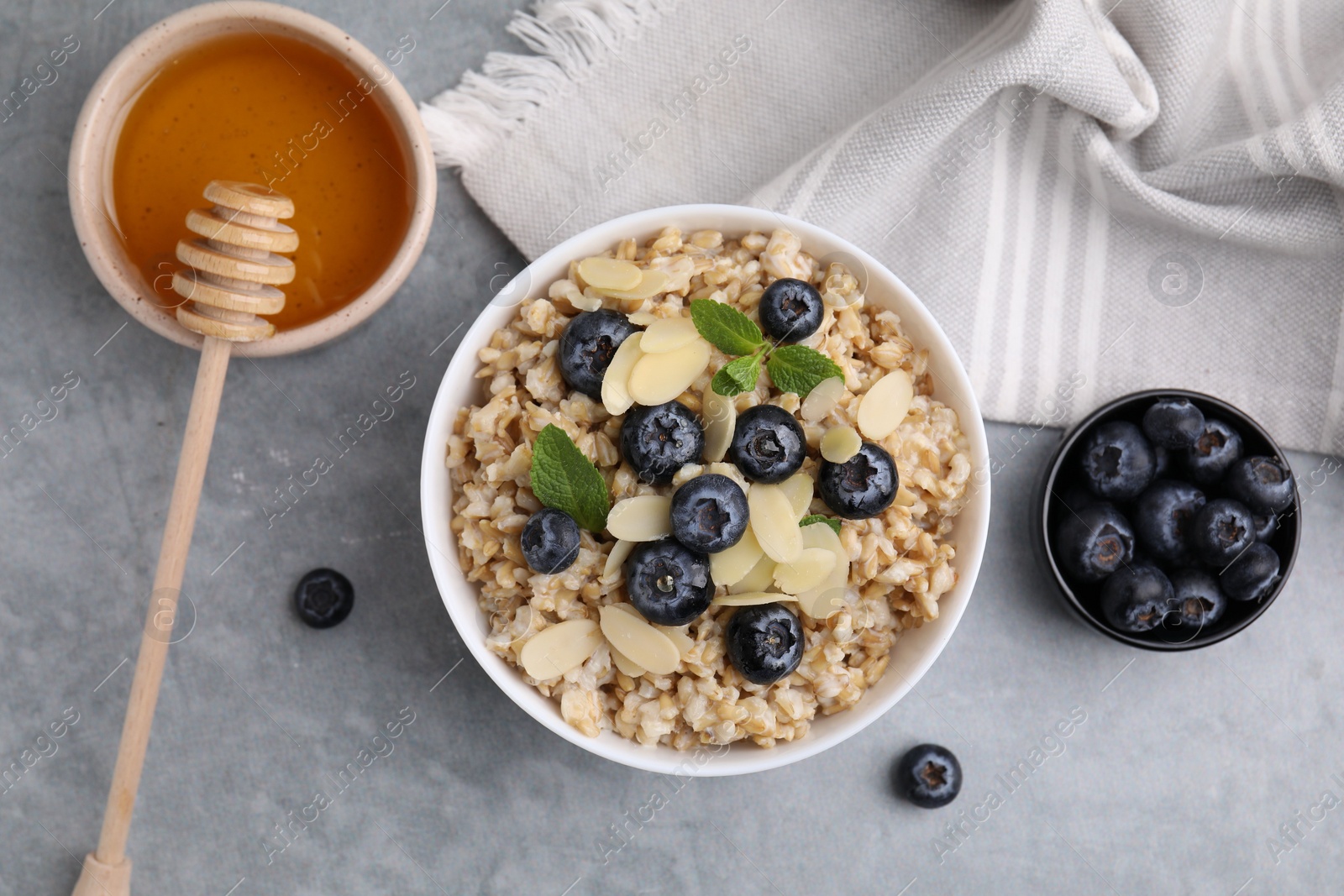 Photo of Tasty oatmeal with blueberries, mint and almond petals in bowl on grey table, flat lay