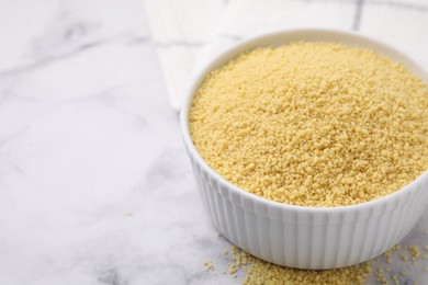 Raw couscous in bowl on light table, closeup. Space for text