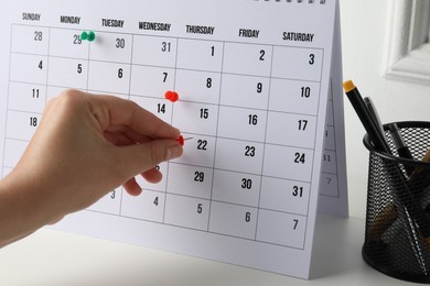 Timetable. Man marking date in calendar with drawing pins at white table, closeup