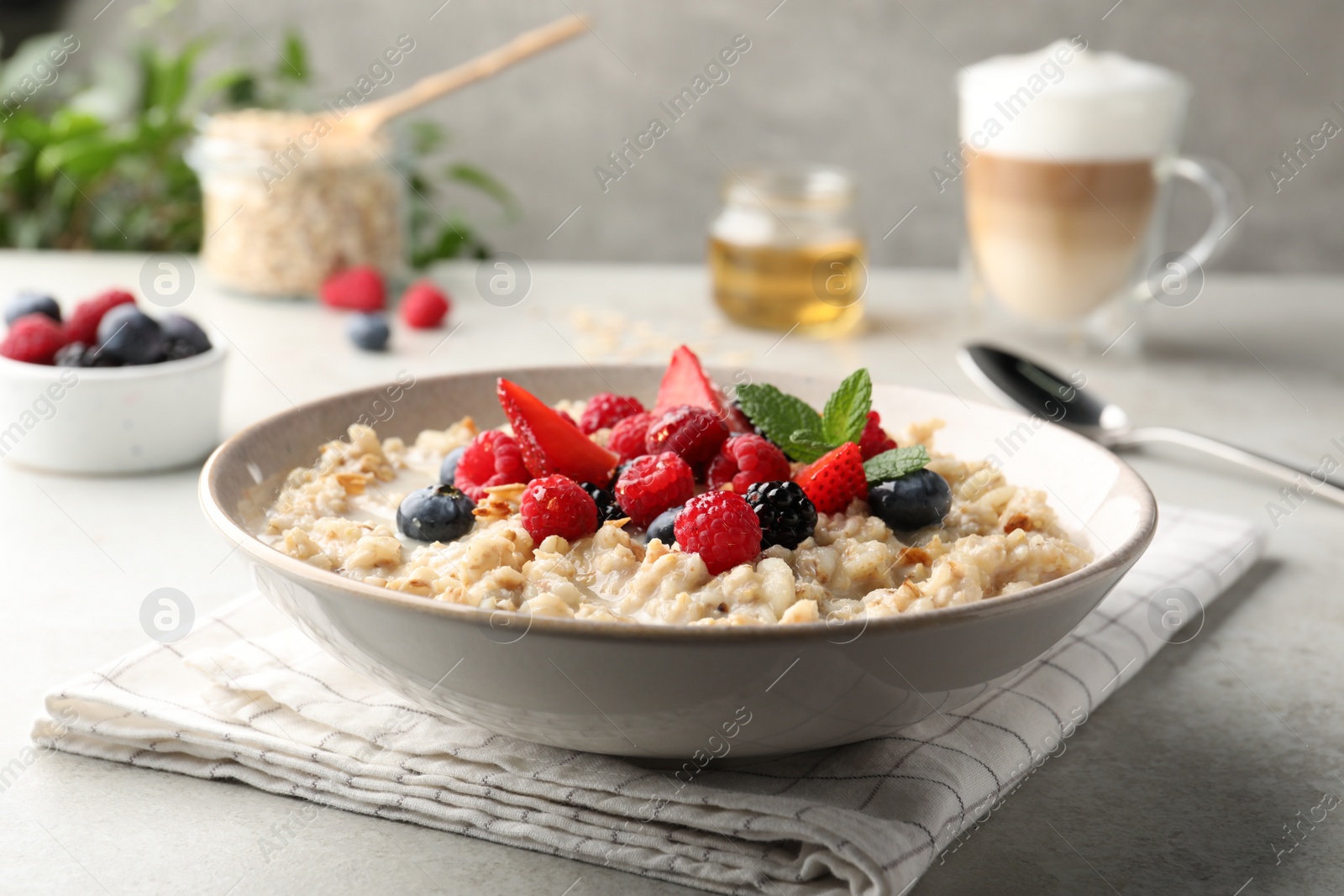 Photo of Bowl of oatmeal porridge served with berries on light grey table, closeup