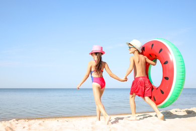 Cute little children with inflatable ring at beach on sunny day