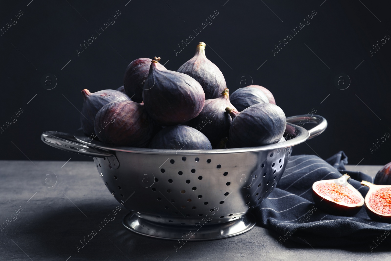 Photo of Colander with fresh ripe figs on table against black background