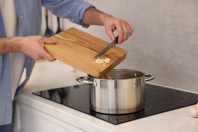 Man adding garlic into soup in kitchen, closeup