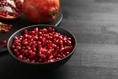 Photo of Tasty ripe pomegranates and grains on dark wooden table. Space for text