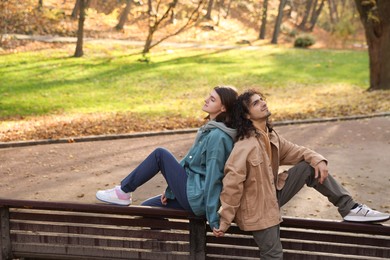 Photo of Young couple sitting on wooden bench in autumn park. Dating agency