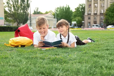 Children with school stationery reading book on green lawn outdoors