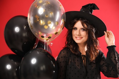 Beautiful woman in witch costume with balloons on red background. Halloween party