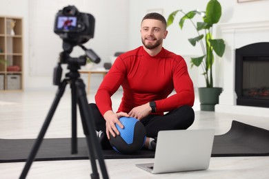 Photo of Trainer with ball recording fitness lesson on camera at home