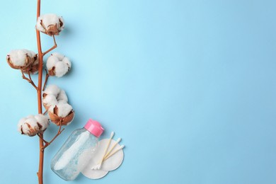 Bottle of makeup remover, cotton flowers, pads and swabs on light blue background, flat lay. Space for text