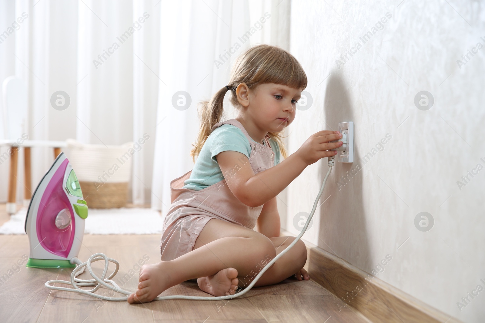 Photo of Little child playing with electrical socket and iron plug at home. Dangerous situation