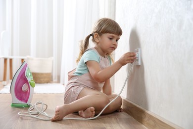 Little child playing with electrical socket and iron plug at home. Dangerous situation