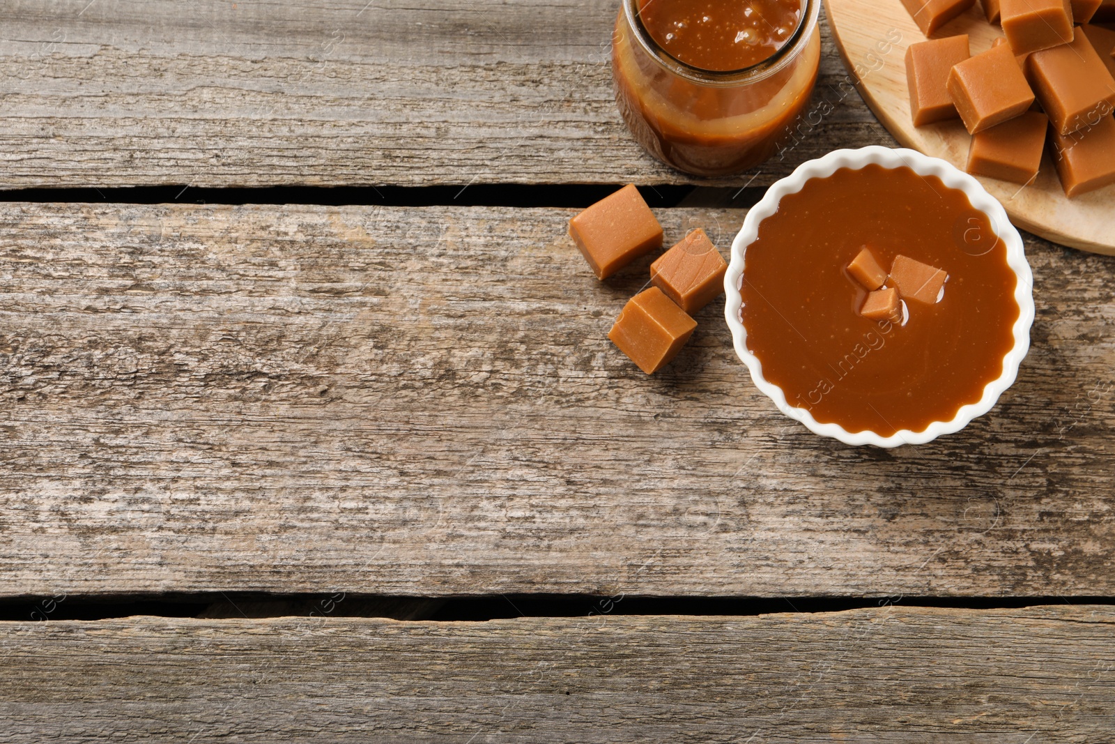 Photo of Tasty salted caramel and candies wooden table, flat lay. Space for text