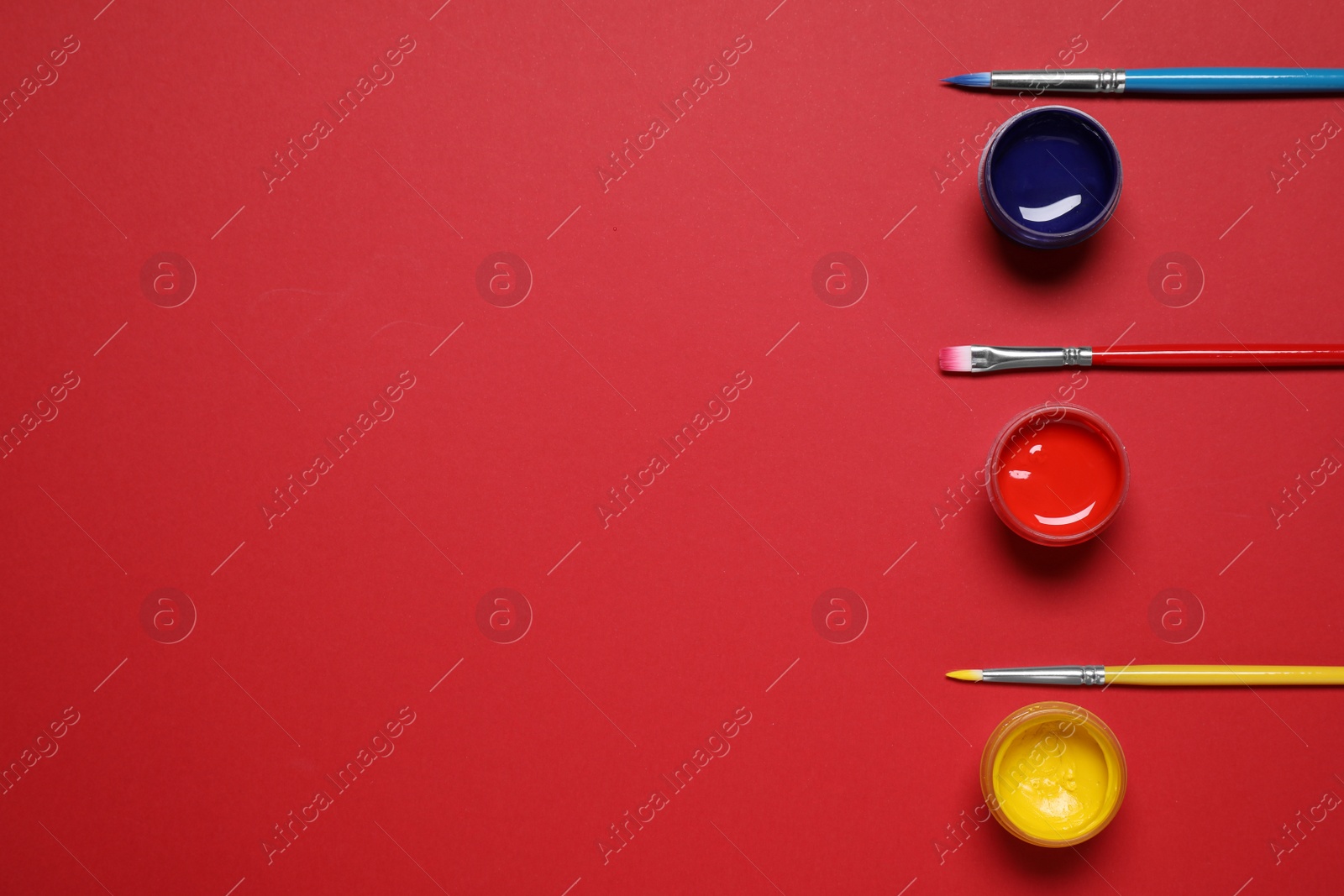 Photo of Brushes and jars with paint on red background, flat lay. Space for text