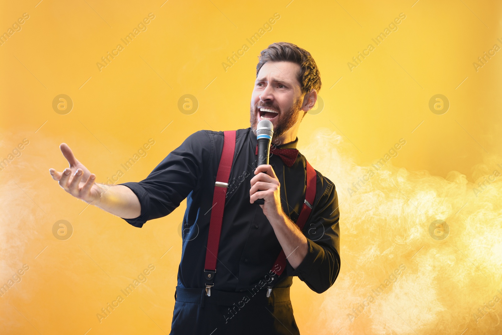 Photo of Emotional man with microphone singing on yellow background