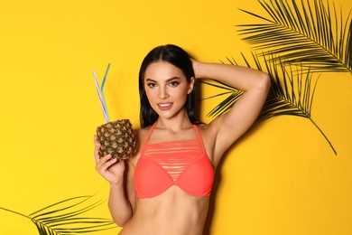 Photo of Beautiful young woman in stylish bikini with cocktail and tropical leaves on yellow background