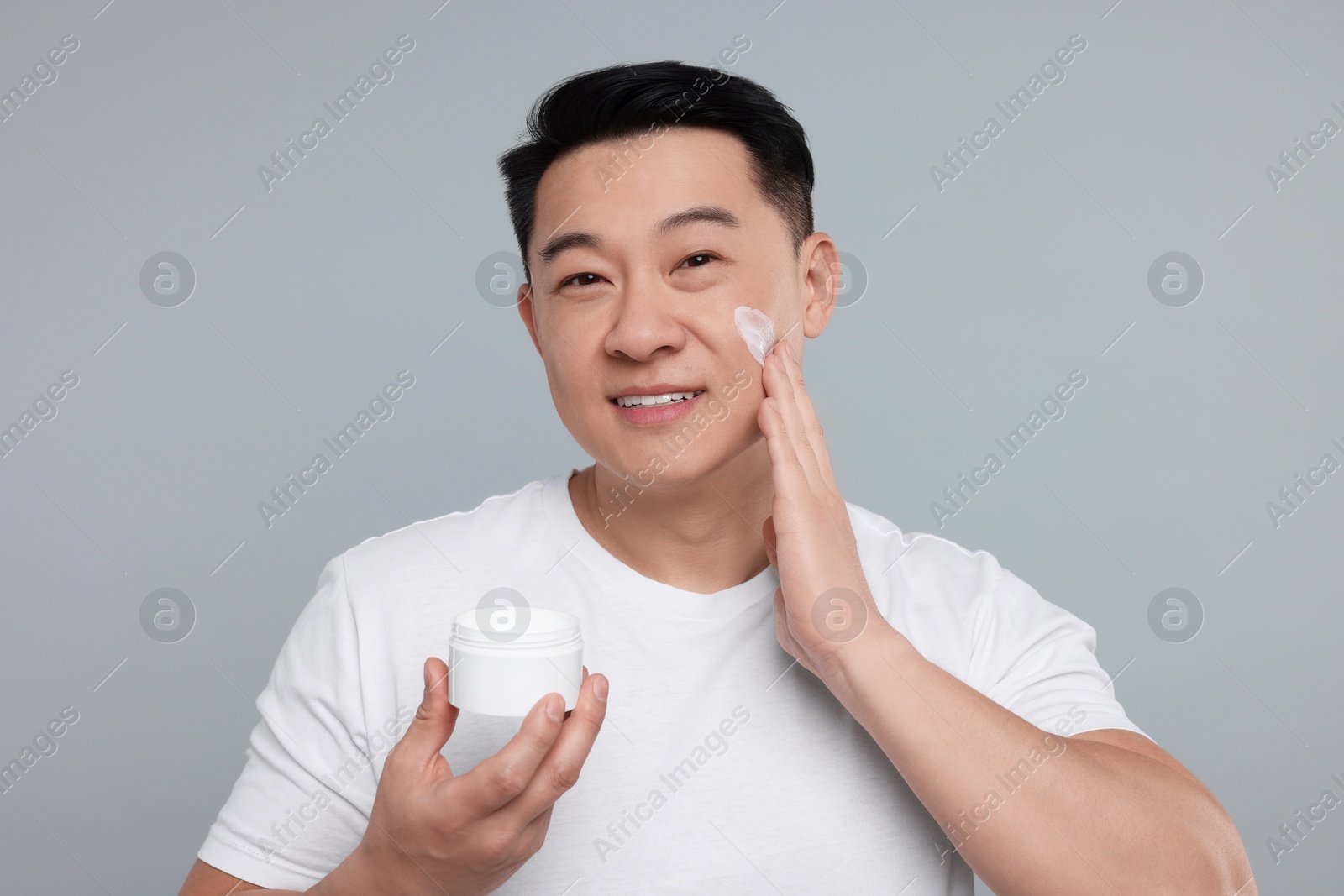 Photo of Handsome man applying cream onto his face on light grey background