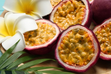 Photo of Halves of passion fruits (maracuyas), palm leaf and flowers on wooden plate, closeup