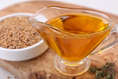 Photo of Jug of natural oil and mustard seeds on wooden table, closeup