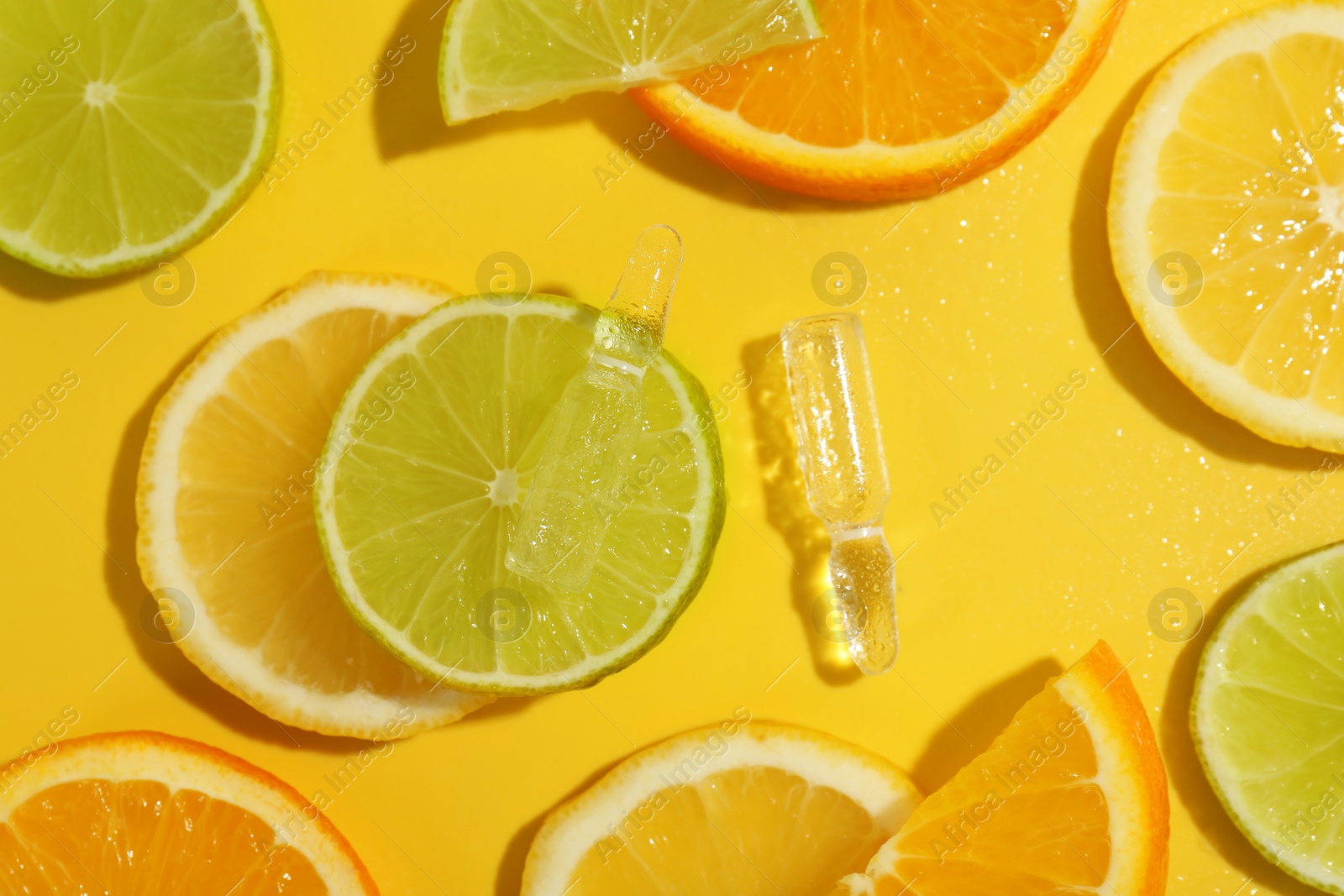 Photo of Skincare ampoules with vitamin C and citrus slices on yellow background, flat lay