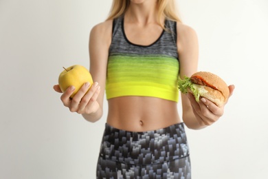 Photo of Woman holding tasty sandwich and fresh apple on light background. Choice between diet and unhealthy food