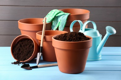 Photo of Many terracotta flower pots with soil and gardening tools on light blue wooden table