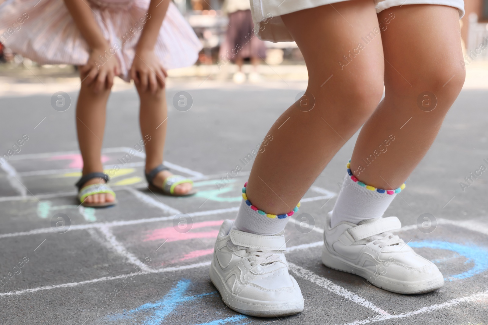 Photo of Little children playing hopscotch drawn with chalk on asphalt outdoors, closeup