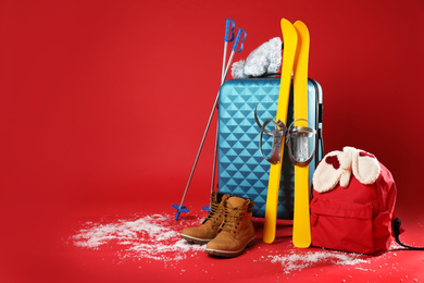 Suitcase with warm clothes and skis on red background, space for text. Winter vacation