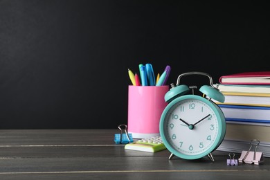 Photo of Alarm clock and different stationery on wooden table near blackboard, space for text. School time