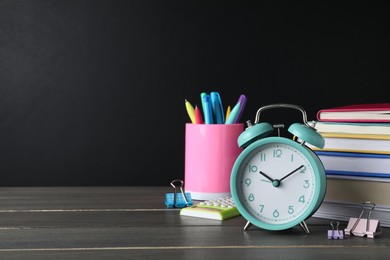 Alarm clock and different stationery on wooden table near blackboard, space for text. School time