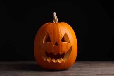 Scary jack o'lantern made of pumpkin on wooden table against black background. Halloween traditional decor