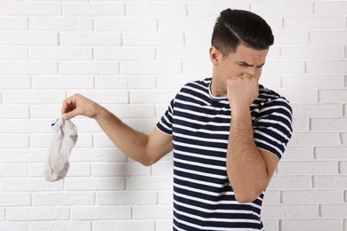 Man feeling bad smell from dirty socks near white brick wall