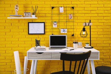 Stylish home office interior with comfortable workplace near yellow brick wall