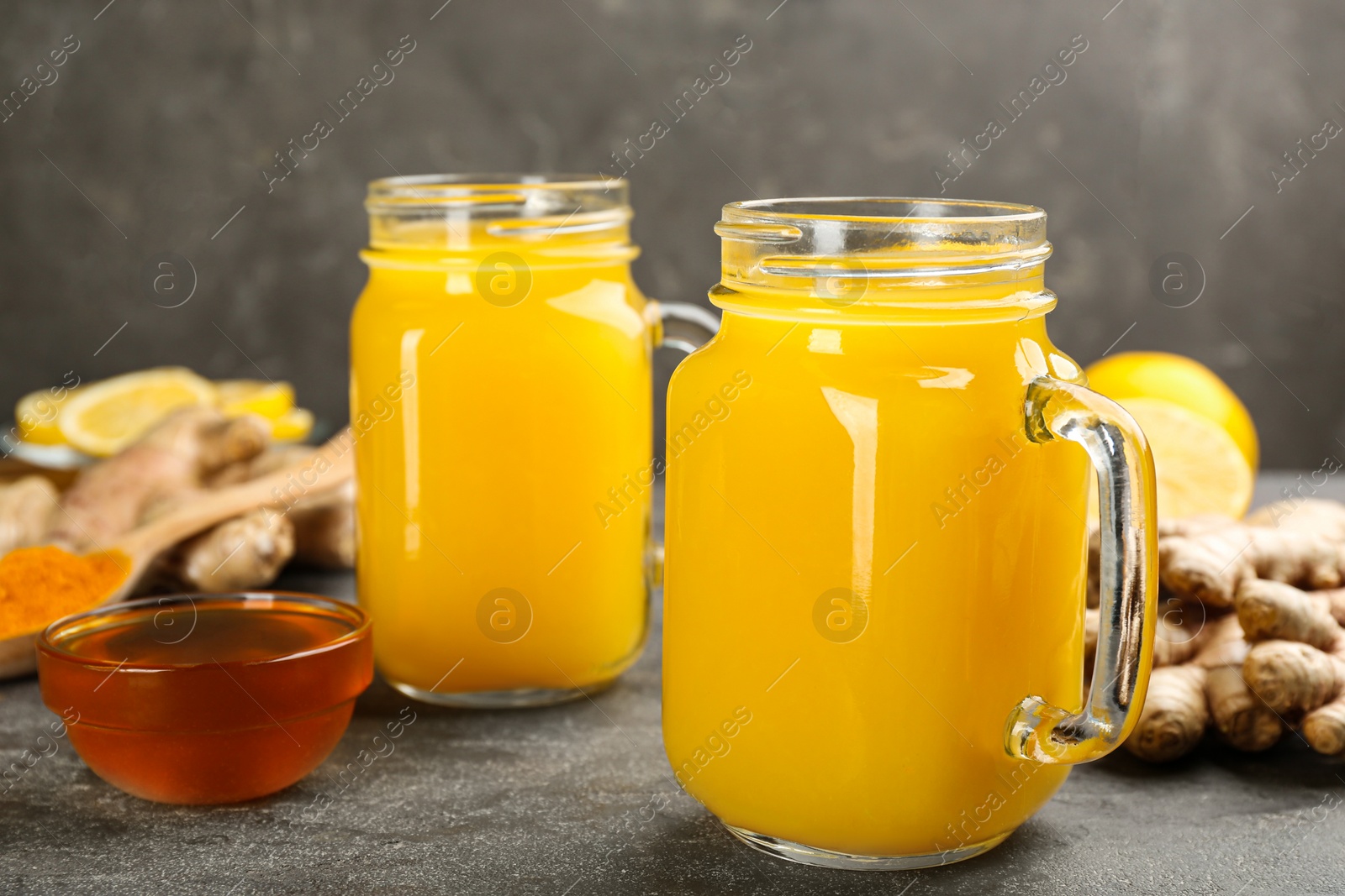 Photo of Two mason jars of immunity boosting drink and ingredients on grey table, closeup