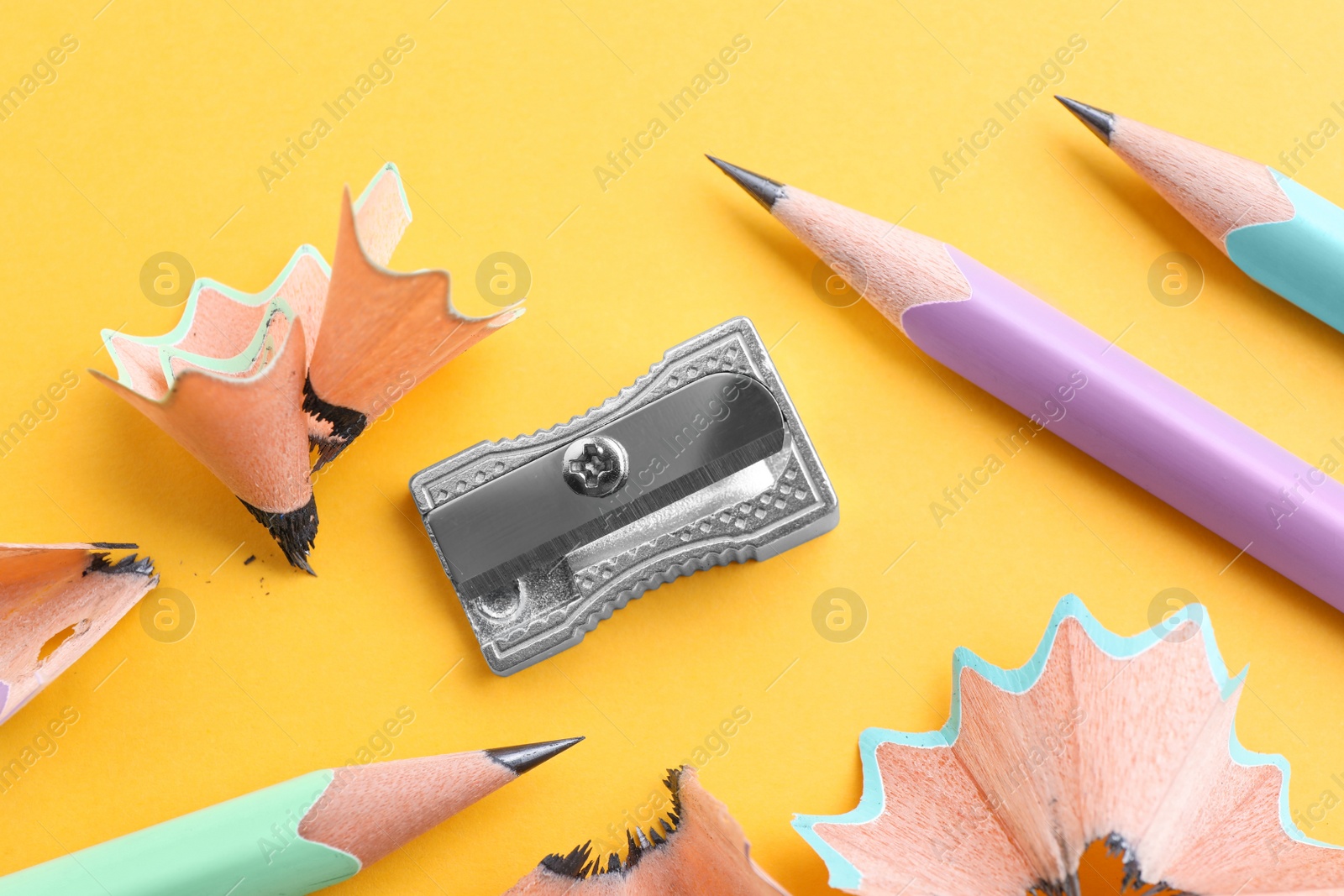 Photo of Pencils, sharpener and shavings on yellow background, flat lay