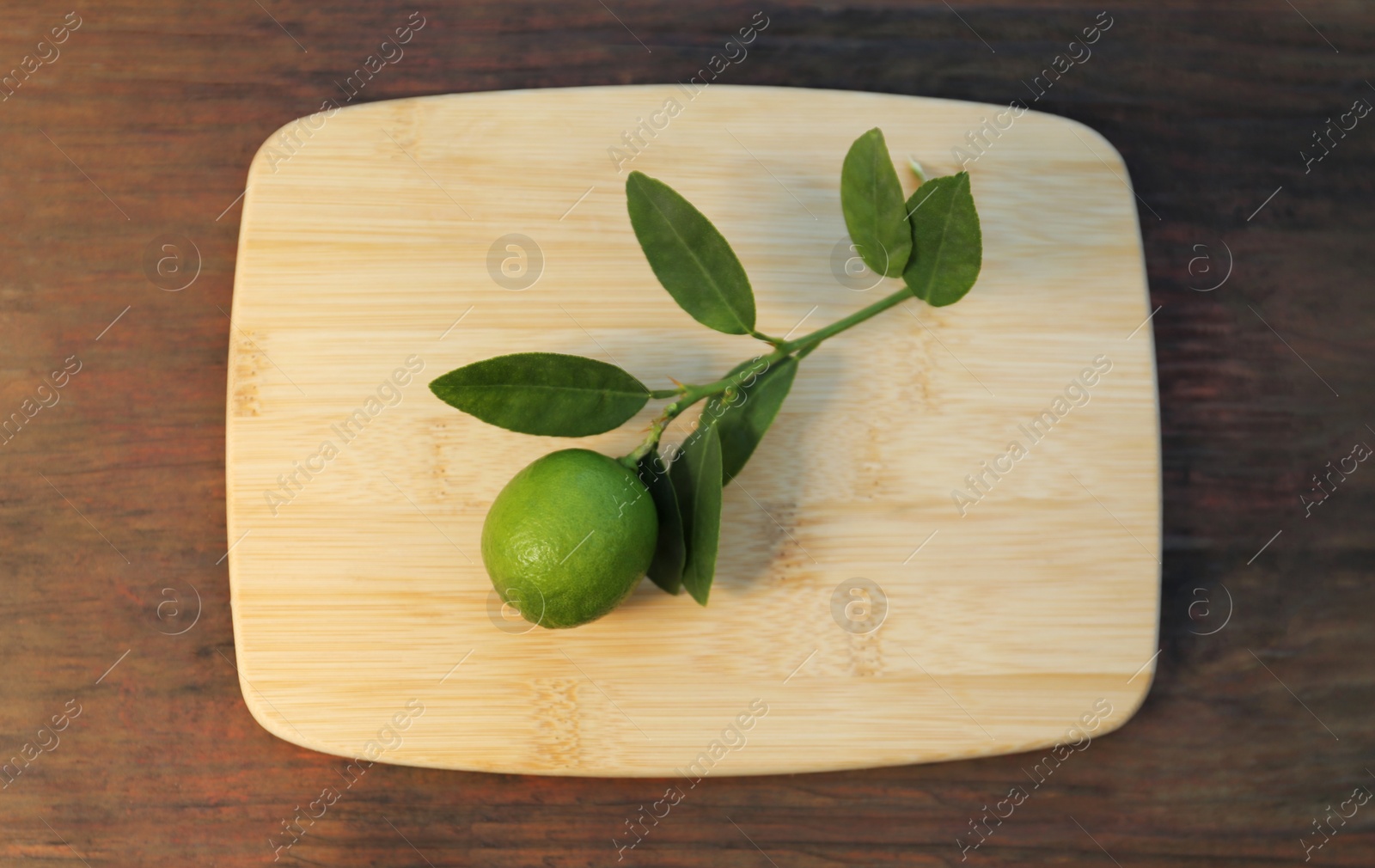 Photo of Board with fresh lime and leaves on wooden table, top view