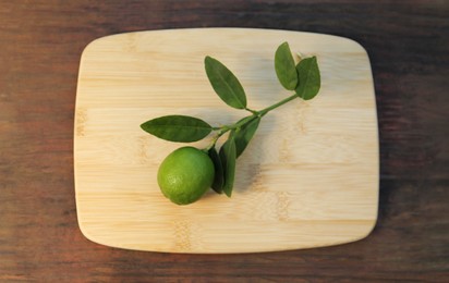 Photo of Board with fresh lime and leaves on wooden table, top view