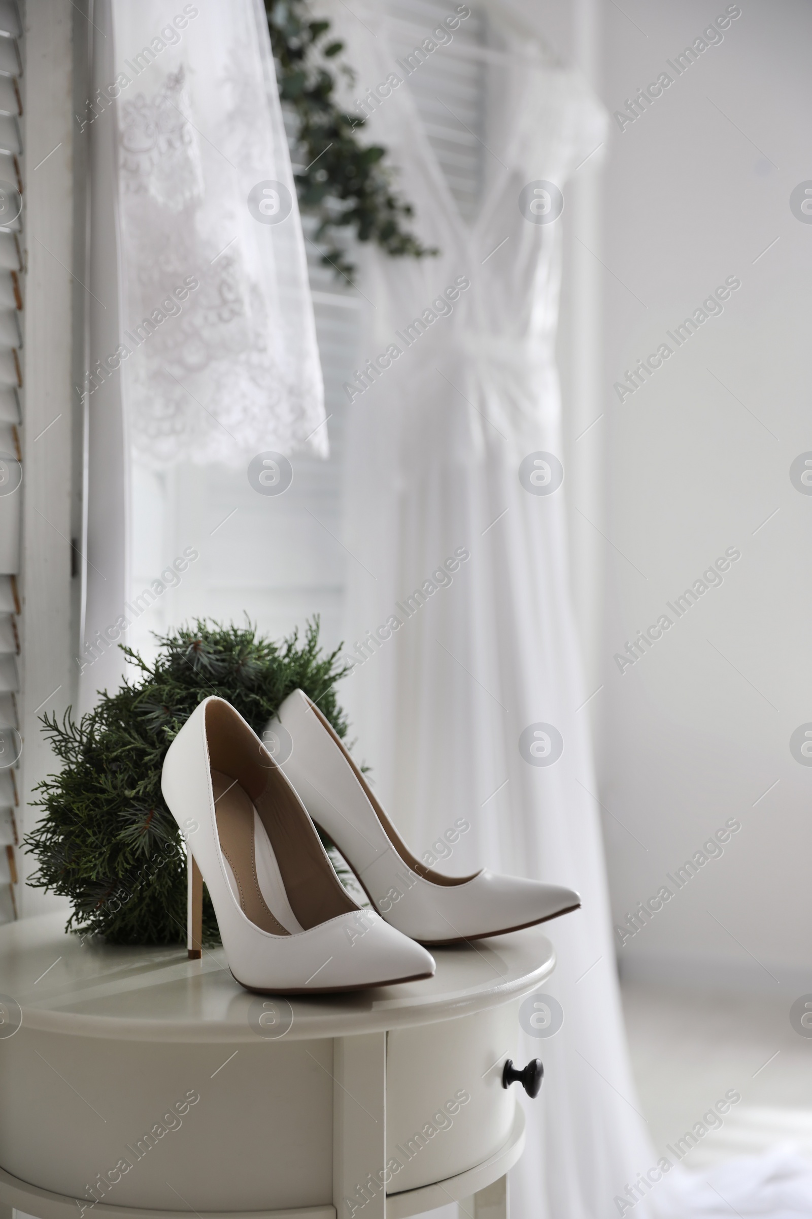 Photo of Pair of white high heel shoes, wreath and blurred wedding dress on background, space for text