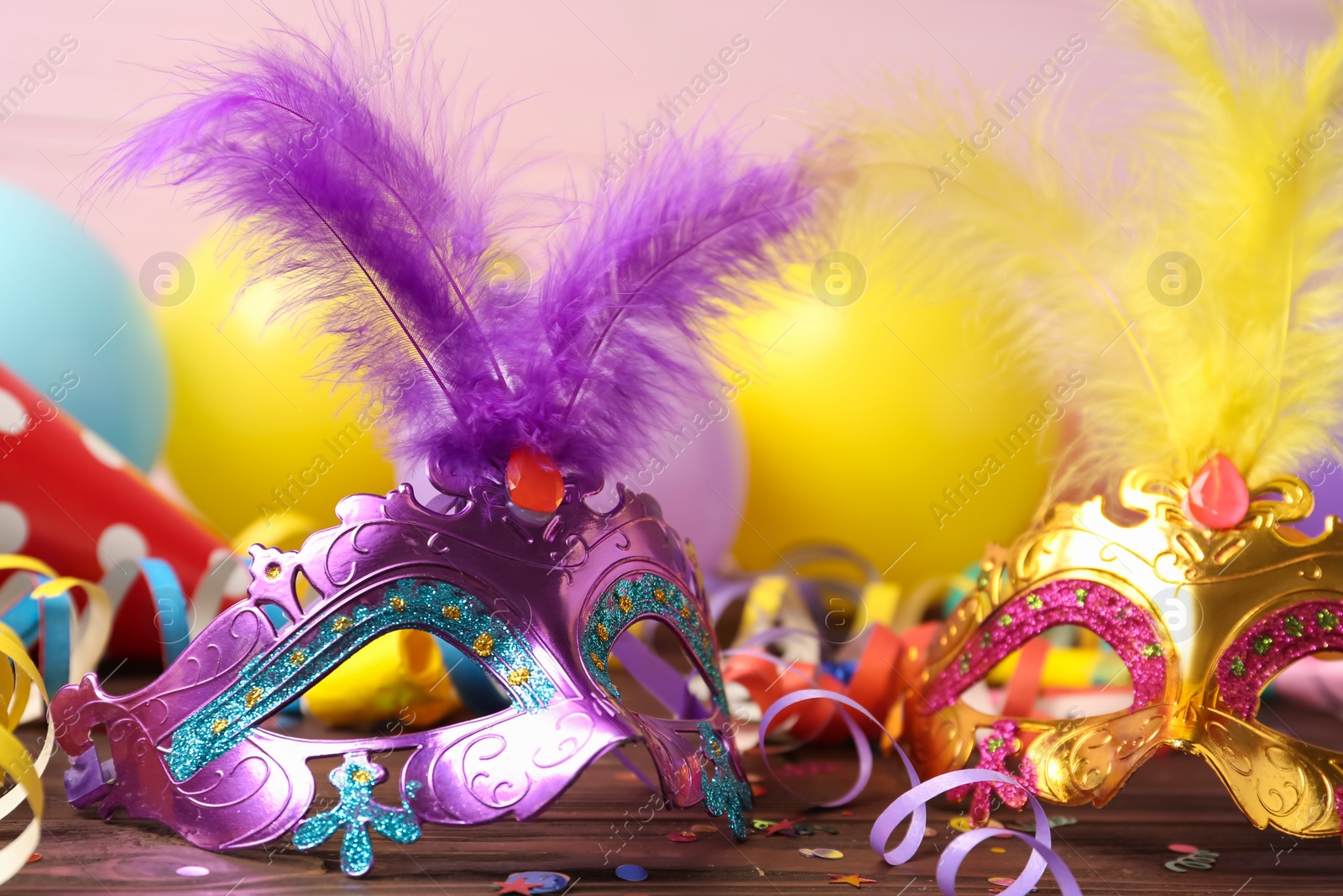 Photo of Beautiful carnival masks and party decor on wooden table, closeup