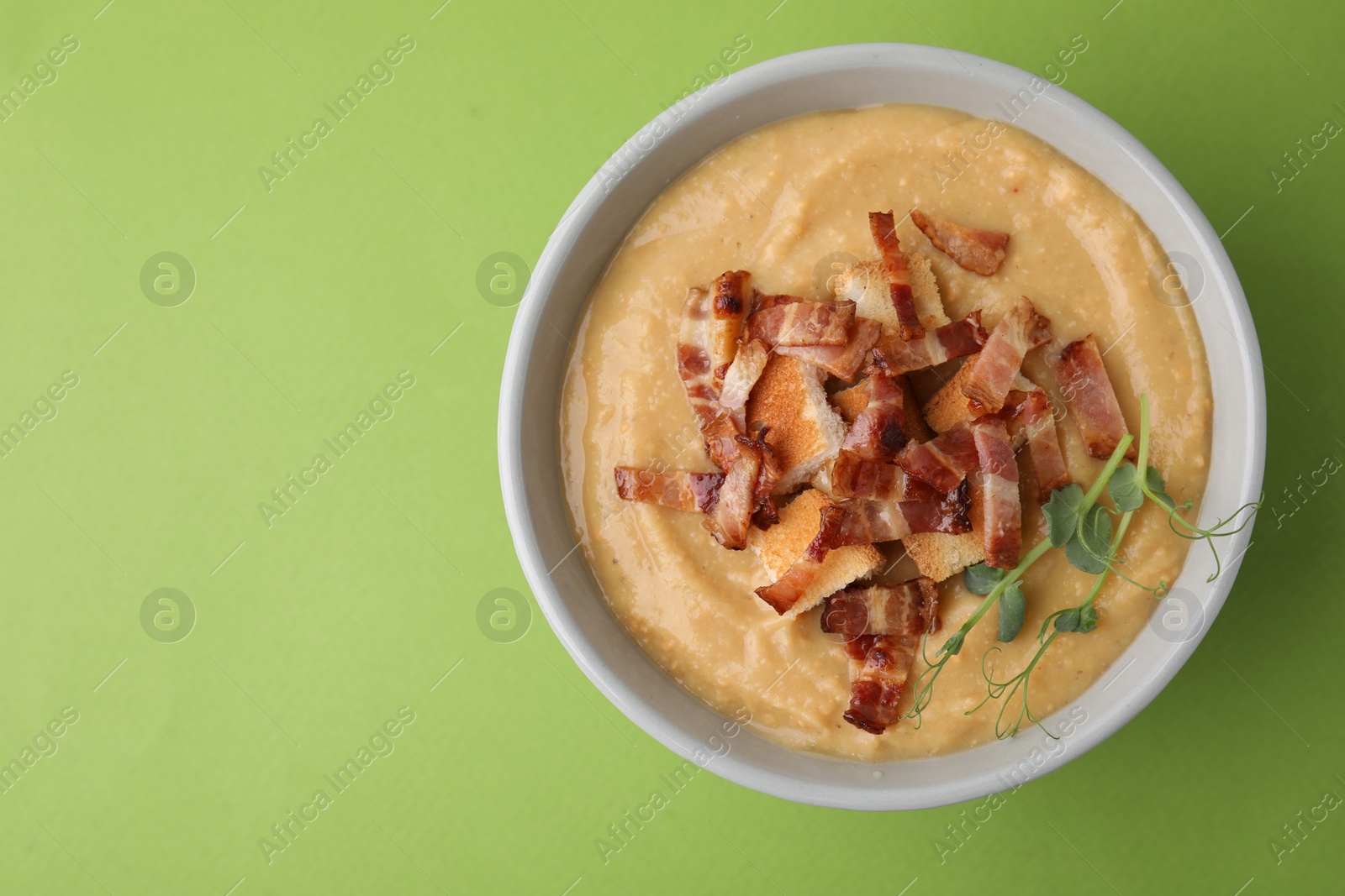 Photo of Delicious lentil soup with bacon and croutons on green background, top view. Space for text