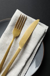 Photo of Elegant golden cutlery, napkin and plate on black background, top view