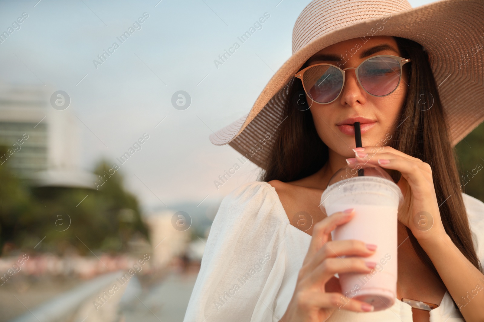 Photo of Beautiful young woman with tasty milk shake outdoors, space for text